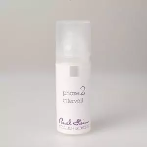 Eine kleine, zylindrische, weiße Flasche mit mattiertem Deckel und der Aufschrift „intervall Avocadoöl parfümfrei 50ml Phase 2“ in violetter Schrift. Der Produktaufdruck auf der Unterseite lautet „Ruel Heim nature + science“. Die Flasche steht auf einem schlichten, hellgrauen Hintergrund.